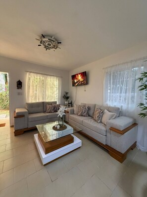 A living room with two sofas, a coffee table, a TV, and a ceiling fan. - Family 2BR Townhouse Beach Access, Pool & Fast Wi-fi (Punta Cana)