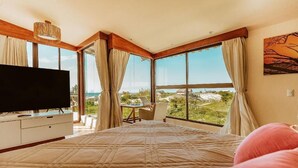 Ein Schlafzimmer mit einem großen Bett, einem Fernseher, einem Schreibtisch und Blick ins Freie.