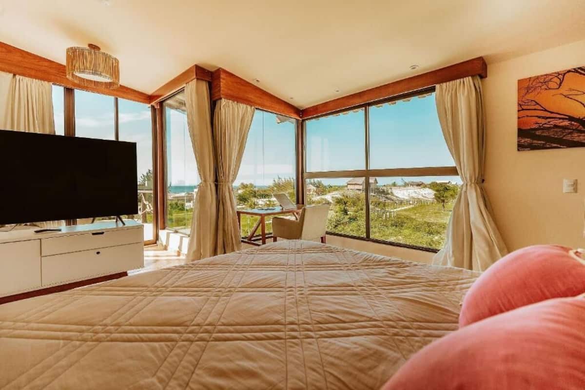 A bedroom with a large bed, a TV, a desk, and a view of the outdoors.