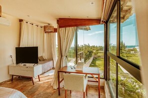 A room with a bed, a TV, a table, and a view of a landscape. - Vila Harmonia (Cruz)