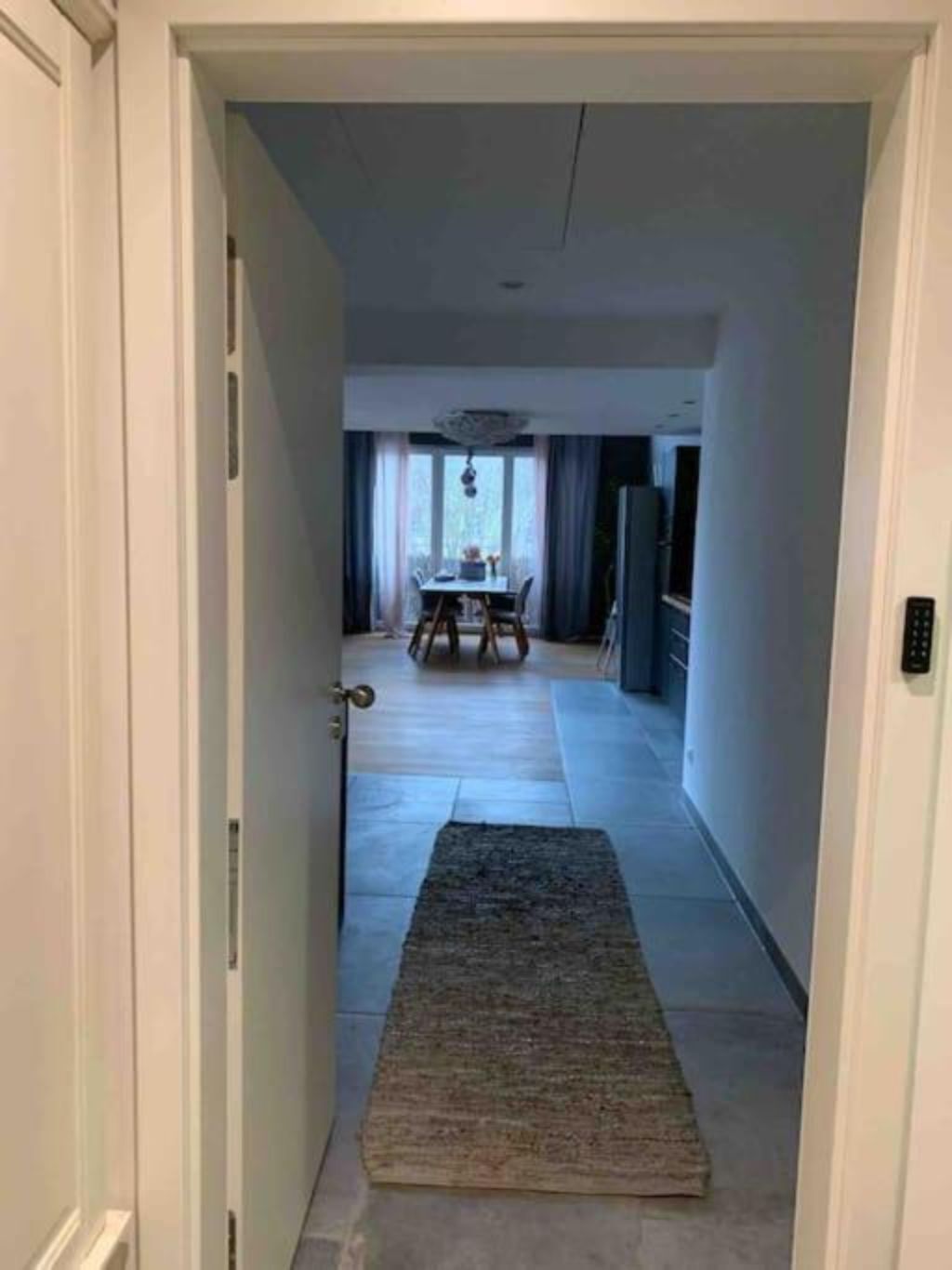 A hallway leading to a dining area with a table and chairs, a rug on the floor, and a ceiling light fixture.