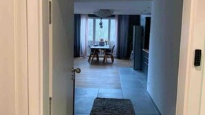 Un passadís condueix a una zona de menjador amb una taula i caires, una catifa al sòl i un llum de sostre.
