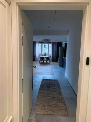 Ein Flur, der in einen Essbereich mit Tisch und Stühlen führt, mit einem Teppich auf dem Boden und einer Deckenleuchte.