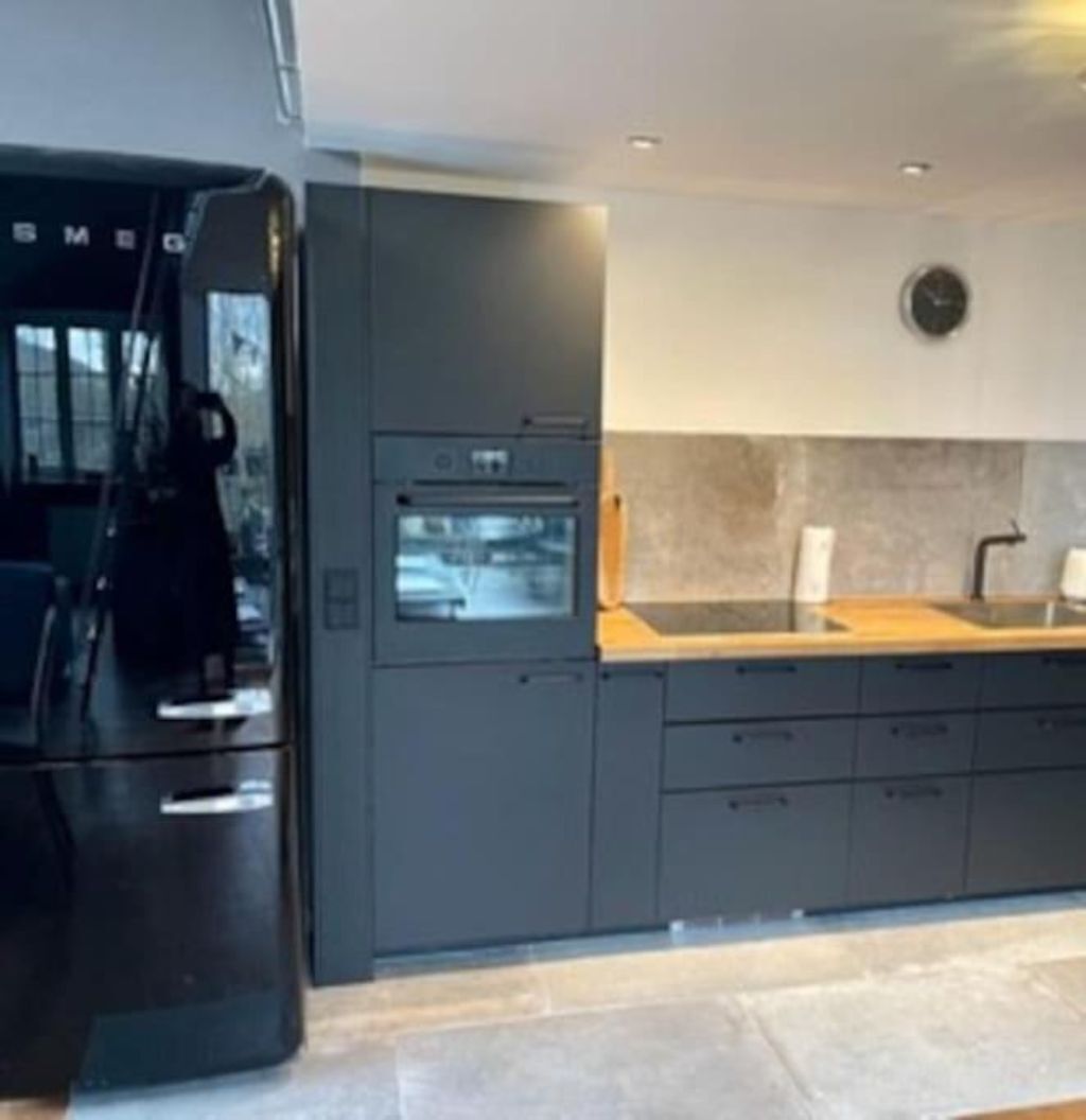 A modern kitchen with a built-in oven, a sink, and a clock on the wall.