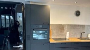 Una cuina moderna amb forn de mur, un rentamànega i un rellotge a la paret.