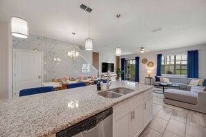 A modern kitchen with granite countertops, a built-in dishwasher, and a dining area with blue chairs. - SL4895 - 5BR house with pool near Disney area (Kissimmee)