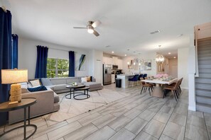 A modern living room with a sofa, coffee table, and a dining area with chairs and a table set for a meal. - SL4895 - 5BR house with pool near Disney area (Kissimmee)