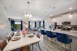 A modern kitchen with a central island, bar seating, and a dining area with a large table set for six. - SL4895 - 5BR house with pool near Disney area (Kissimmee)