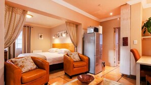 Habitación de hotel con dos sillones de cuero, una cama, una mesa de centro de madera, un refrigerador y una zona de comedor.