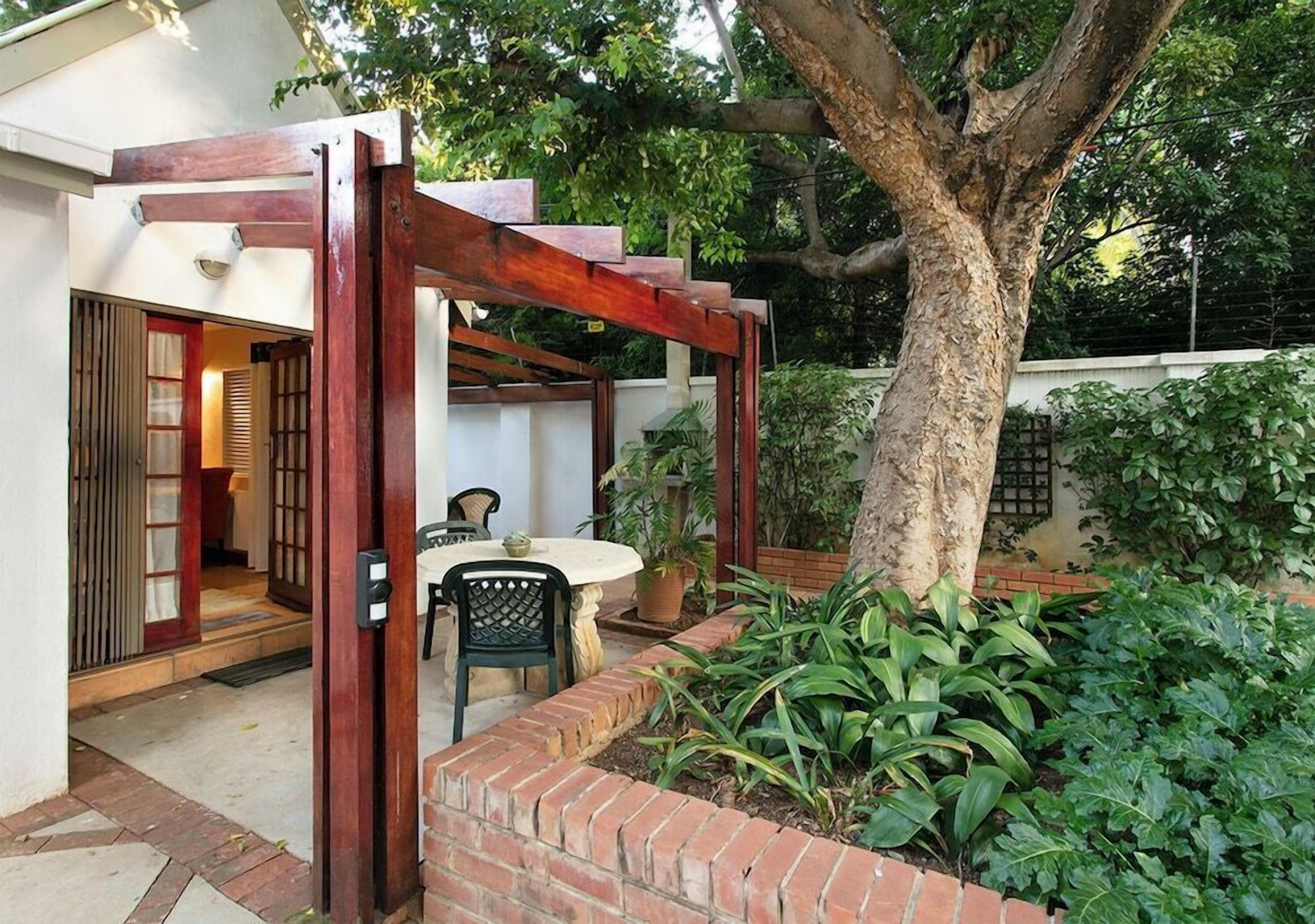 A patio with a table and chairs, a wooden pergola, and a brick planter with greenery.