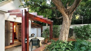 Un patio con una mesa y sillas, una pérgola de madera y una jardinera de ladrillo con plantas.