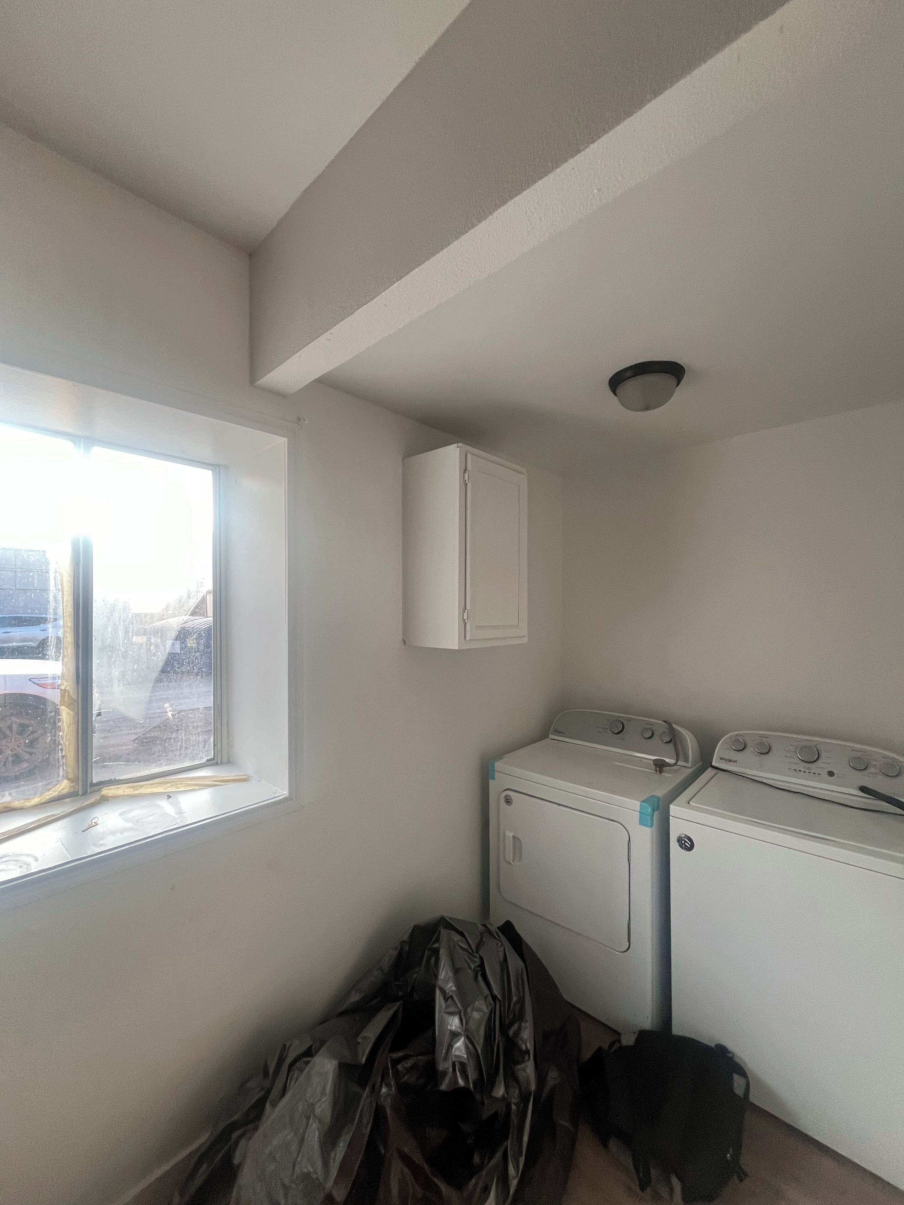 A laundry room with a washing machine and dryer, a window, and a ceiling light fixture.