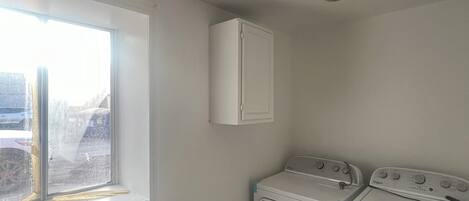A laundry room with a washing machine and dryer, a window, and a ceiling light fixture.