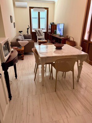 Ein Wohnzimmer mit Esstisch, Stühlen, einer Couch, einem Fernseher und einem Kühlschrank.