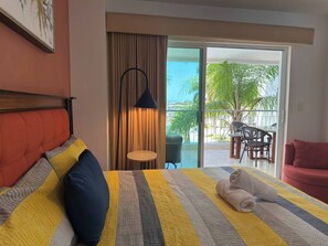 A hotel room with a bed, a red sofa, a small table, and a view of the outdoors. - Costa Veleros, Atardeceres Únicos by GPS (Mazatlán)