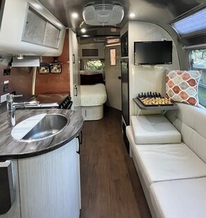 Ein kompaktes Wohnmobil-Interieur mit Küchenzeile, einer Sitzecke mit Schachbrett und einem darüber montierten Fernseher.
