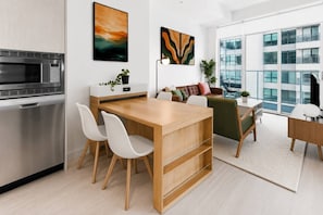 Une cuisine moderne dotée d’un four à micro-ondes encastré, d’un coin repas avec des chaises et offrant une vue sur un immeuble en verre.