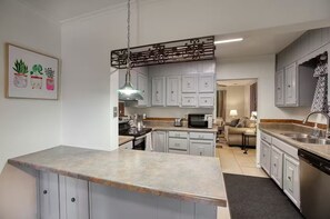 Eine Küche mit weißen Schränken, einer Granitabdeckung, einer Hängeleuchte und einem Essbereich mit einer Couch und einem Tisch.
