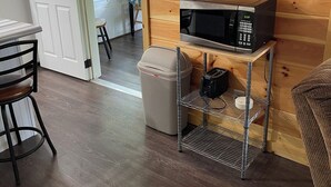 Un intérieur en bois avec un four à micro-ondes posé sur une étagère, une poubelle et une porte donnant sur l’extérieur.