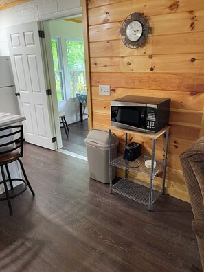 A wooden interior with a microwave on a shelf, a trash bin, and a door leading outside.