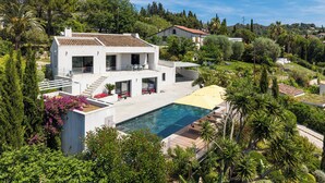 Ein modernes, zweistöckiges Haus mit Swimmingpool, umgeben von üppigem Grün und Bäumen.