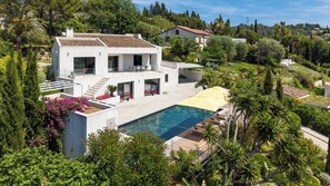 A modern two-story house with a swimming pool, surrounded by lush greenery and trees.