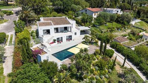 Ein modernes, zweistöckiges Haus mit Swimmingpool, umgeben von üppiger Vegetation und Palmen.