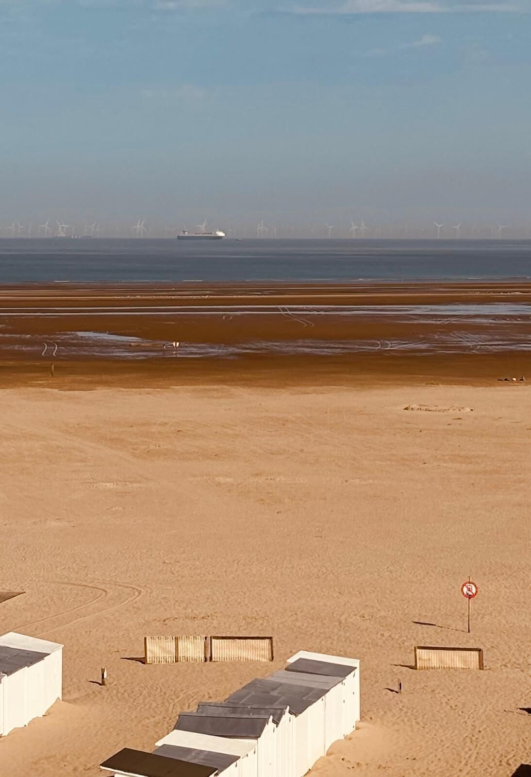 View of the sandy beach with white cabins and a distant ship on the calm sea