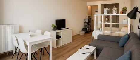 Modern living area with a gray sectional sofa and a white dining table for four.