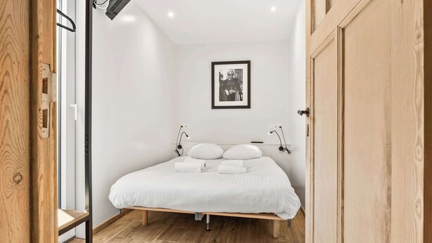 Un dormitorio con una cama, ropa de cama blanca, un cuadro enmarcado en la pared y una puerta de madera.