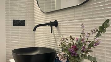 Un baño con un lavabo negro tipo cuenco, un espejo, un florero con flores y un insecto decorativo.