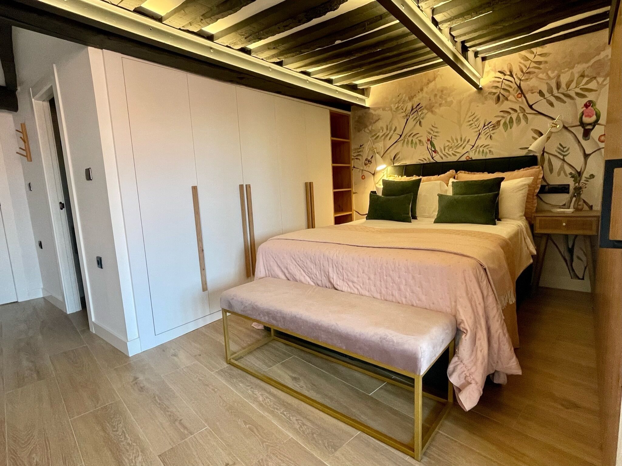 A bedroom with a bed, a bench, a wardrobe, and a wall with a leaf pattern.
