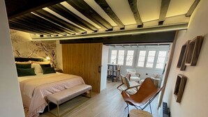A bedroom with a bed, bench, wooden floor, and a dining area with chairs and a table. - MAGDALENA APARTMENT (Oviedo)
