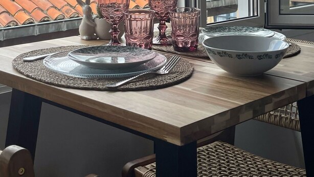 A dining table with placemats, cutlery, and pink glassware, set against a window overlooking a tiled roof. - MAGDALENA APARTMENT (Oviedo)