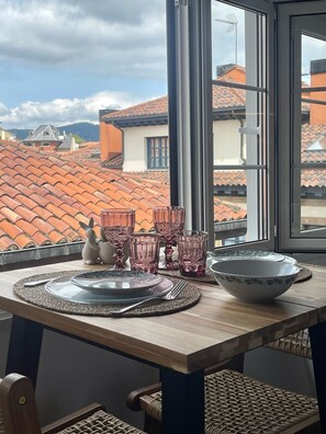 A dining table with placemats, cutlery, and pink glassware, set against a window overlooking a tiled roof. - MAGDALENA APARTMENT (Oviedo)