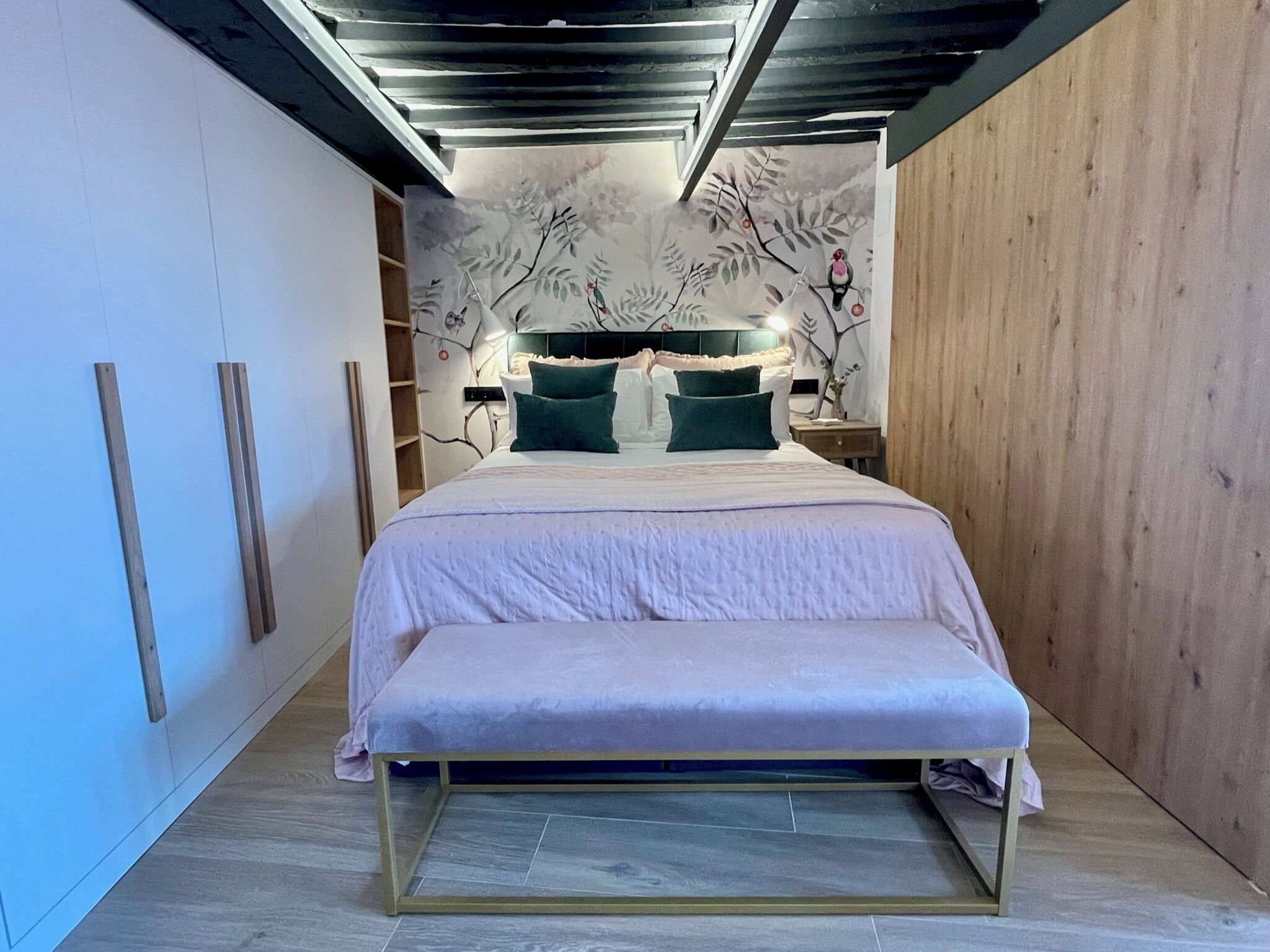 Une chambre à coucher avec un lit, des tables de chevet et un mur décoré d’une fresque représentant un arbre.