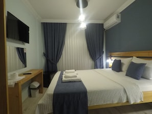 A hotel room with a bed, a desk, a TV, and an air conditioning unit. - gökçeada helios pansiyon (Gokceada)