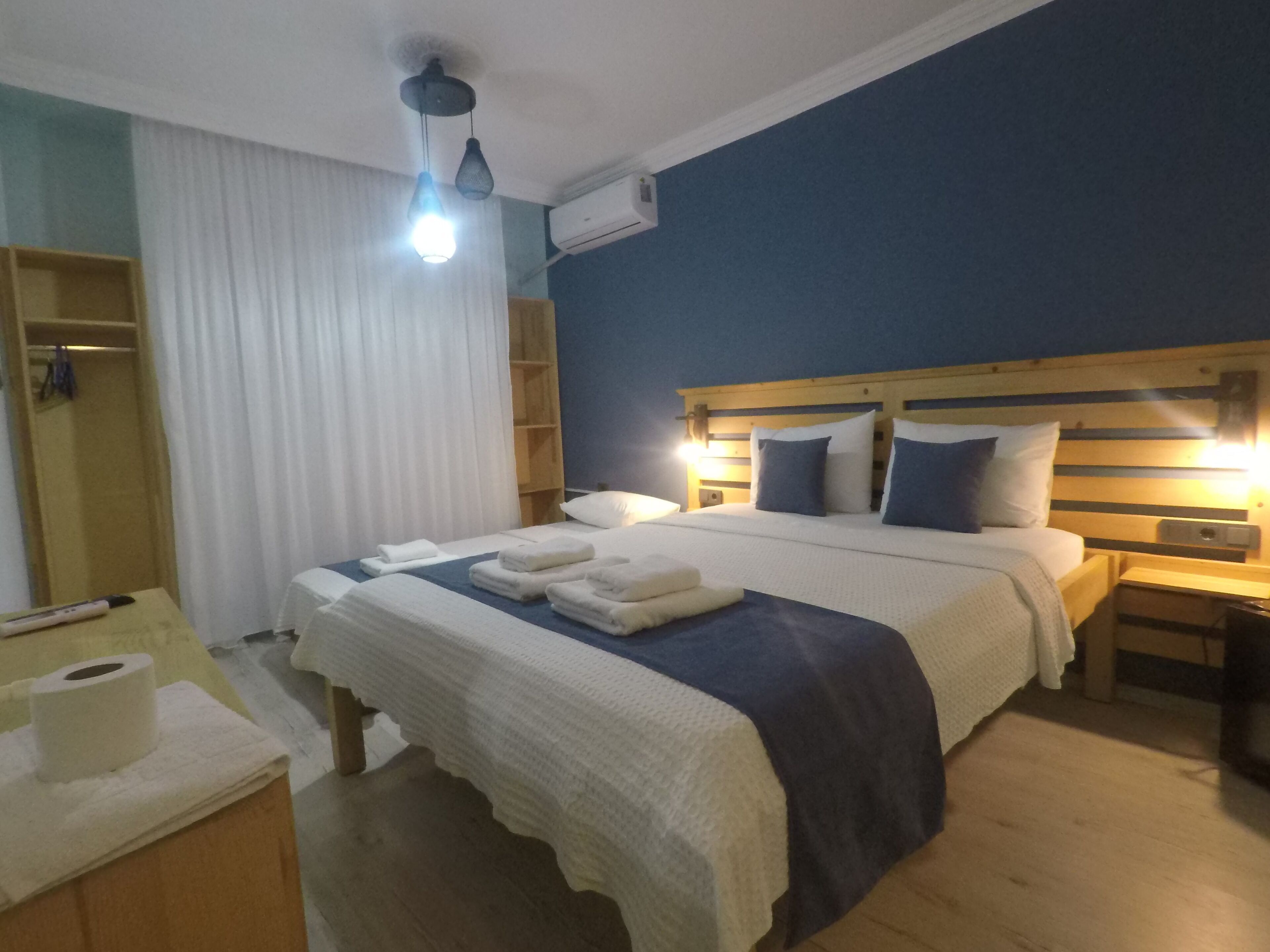 A hotel room with a large bed, bedside tables, a wardrobe, and a ceiling light fixture.