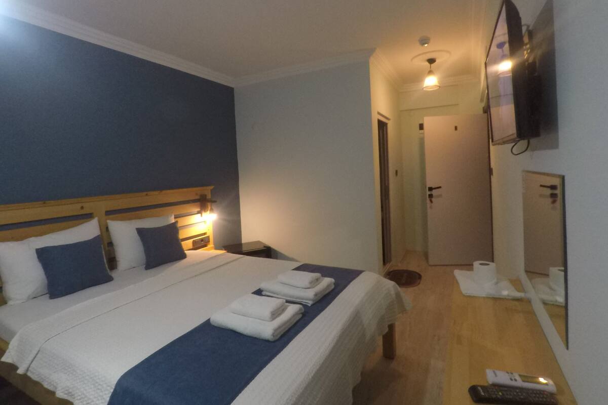 A hotel room with a bed, bedside tables, a TV, a mirror, and a bathroom door.