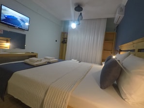 A hotel room with a bed, a TV mounted on the wall, a ceiling fan, and a window with curtains. - gökçeada helios pansiyon (Gokceada)