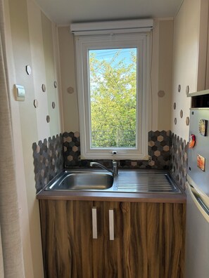 A compact kitchen with a window, a sink, and wooden cabinets. - 3 bedroom mobile home - Les Salins de la Gardiole - Vic-la-Gardiole (Vic-la-Gardiole)