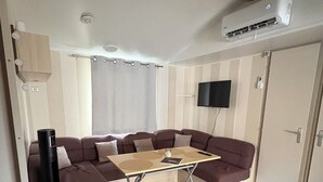 Kompakti olohuone, jossa on sohvaryhmä, pieni pöytä, seinälle asennettu televisio ja ilmastointilaite.