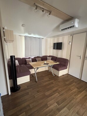 A compact living space with a sofa set, a small table, a TV mounted on the wall, and an air conditioning unit. - 3 bedroom mobile home - Les Salins de la Gardiole - Vic-la-Gardiole (Vic-la-Gardiole)