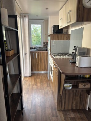 A modern kitchen with wooden cabinets, a gas stove, a microwave, and a toaster. - 3 bedroom mobile home - Les Salins de la Gardiole - Vic-la-Gardiole (Vic-la-Gardiole)
