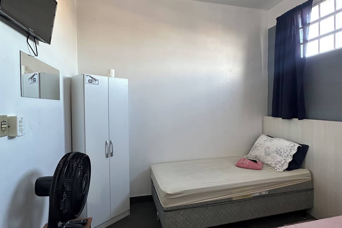 A bedroom with a bed, a desk with a fan, a TV, and a wardrobe.