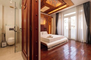 Habitación de hotel con cabina de ducha de vidrio, cama con colchón y almohadas blancas, techo de madera y vistas a través de un ventanal grande.