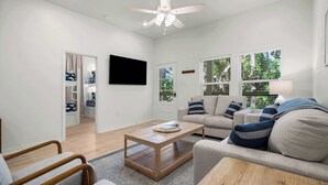 Una sala de estar moderna con un ventilador de techo, un sofá, una mesa de centro y un televisor montado en la pared.