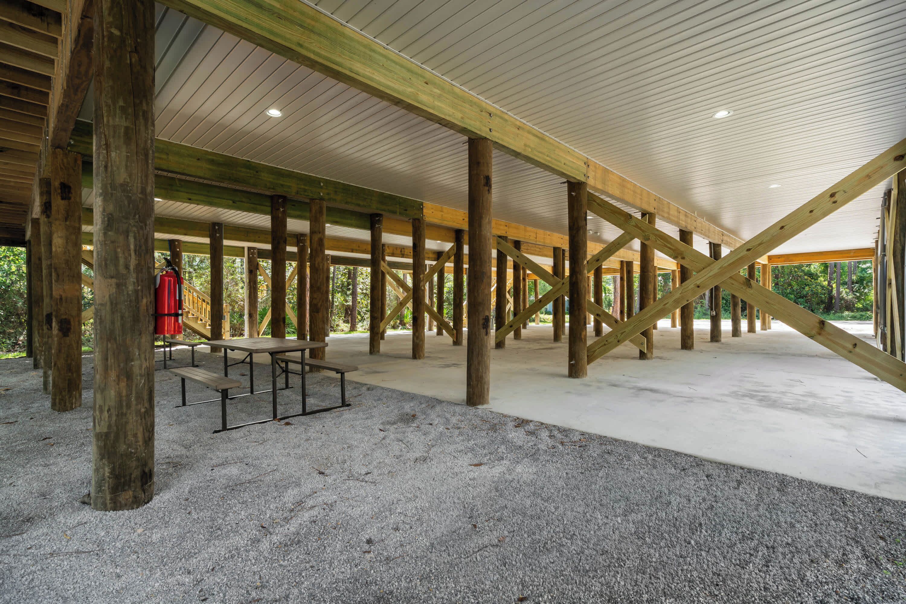 An indoor space with a high ceiling supported by wooden beams, a gravel floor, and a picnic table.