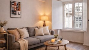 A living room with a sofa, a round coffee table, a lamp, a bookshelf, and a window with a view. - Praça do Comercio Romantic Apartment (Lisboa)
