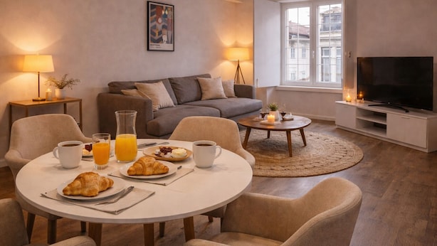 A living room with a dining table set for breakfast, a sofa, a TV, and a window with a view. - Praça do Comercio Romantic Apartment (Lisboa)